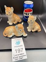 Group view of three lion cub figurines beside soda can for scale