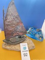 Metal sailboat sculpture beside blue glass wave on yellow surface