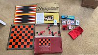 Overview of all game items laid out: backgammon box, checkers board, dominoes box, two Bicycle card decks, jacks, dice, red pouch