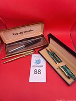 All five writing instruments displayed with two open presentation cases and MaxSold lot card visible