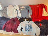 Overview of ten assorted sweatshirts laid out on bed
