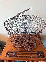Deep round wire basket with hinged rim beside ruler