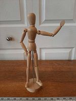Full view of wood mannequin on base with arm raised, ruler for scale