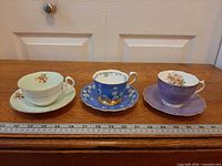 Front view of the three teacup and saucer sets on wooden surface