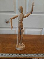Front view of wooden articulated mannequin on stand with ruler for scale