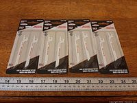Four sealed packs of Briggs & Stratton blades laid out beside ruler