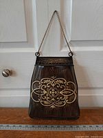 Front view of metal wall pocket showing embossed design and chain