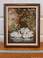 Full view of framed needlepoint showing swans scene and ruler for scale
