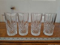 Front view of four matching cut-crystal highball glasses beside ruler for scale