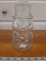Front view of clear glass snowman jar with lid on, ruler for scale