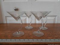 Four Libbey Bravura martini glasses side view showing curved stems and bases beside ruler