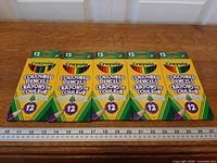 Five sealed Crayola 12-count coloured pencil packs aligned on table with ruler for scale