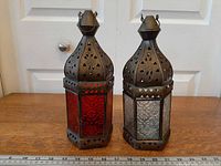 Two brass lanterns side by side showing red and clear glass panels with ruler for scale