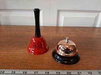 Red hand bell and rose-gold desk bell side by side on wood surface
