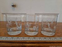 Front view of three etched rocks glasses with Olympic designs next to ruler
