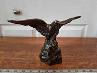 Front view of metal eagle statue showing wings spread and rocky base with ruler for scale