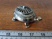 Side view of turtle-shaped silver-tone trinket box beside ruler