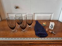 Full lot with 4 glasses, blue bottle tray, corkscrew, cork and box alongside ruler for scale