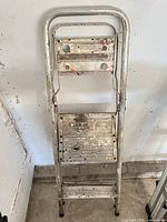Full view of folded two-step ladder showing overall condition and paint splatters