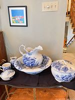 Group shot of all six matching blue floral transferware pieces on a table: pitcher inside basin, covered tureen, lidded dish, creamer, mug