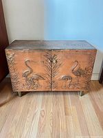 Front view showing embossed copper flamingo panels and brass-toned legs