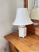Full view of porcelain lamp with shade on wooden dresser
