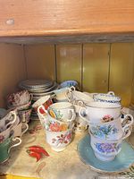 Stacked floral and teal teacups with saucers and dessert plates on shelf