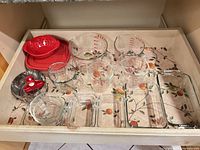 Drawer view of glass measuring cups, glass containers, bowls, steamer basket, red strainer, lids