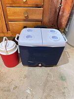 Blue Rubbermaid cooler next to red beverage jug