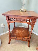 Front view of carved oak Eastlake-style side table showing apron details and lower shelf wear