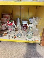 Shelf with assorted glass, ceramic and metal pieces including holiday mugs, stemware, creamer and bottle vases