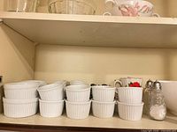 White ribbed ramekins stacked, mugs, shakers visible