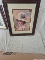 Framed portrait print showing woman in wide-brim hat, cherry frame with gold bead liner