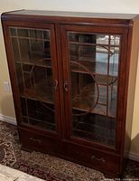 Full view of dark mahogany veneer display cabinet with glass panel double doors and lower drawer