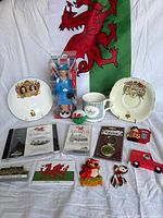 Group shot of all items including flag backdrop, dishware, mug, boxed figure, media, magnets, keyring