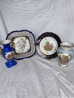 All four Limoges pieces standing together: square bowl, round plate, cobalt vase, light blue vase