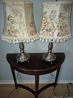 Both brass-tone table lamps with floral shades displayed on table