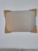 Full view of one mirror mounted on wall showing gold corner ornaments