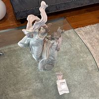Front view of Lladro figurine on glass table with detached broken piece