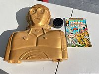 Front view of gold C-3PO carry case front piece, Echo Dot, and Marvel comic