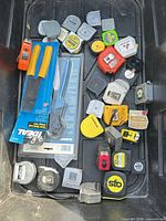 Overview of pliers in packaging and multiple tape measures inside plastic tote