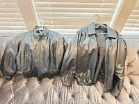 Front view of both black leather jackets displayed side by side on couch
