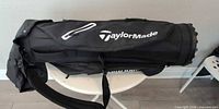 Full length view of black TaylorMade golf bag laid horizontally showing logo, strap and zippered sections