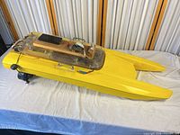 Full side view of yellow RC catamaran hull showing twin bows, acrylic cockpit cover, stern motor
