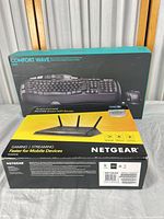 Boxed Logitech Comfort Wave MK550 keyboard and boxed Netgear Nighthawk R6700 router side by side