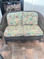 Front view of brown wicker loveseat with tropical print cushions