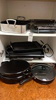 Cookware on cabinet shelf: roasting pan, grill plates, electric griddles, oval roaster and sauté pan