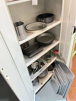 Cabinet showing flour sifter, tart pan, round cake pans, loaf pans, glass jars, cookie cutters
