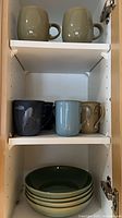 Cabinet showing two green Denby mugs on top shelf, three assorted mugs on middle shelf, four green Denby bowls stacked on bottom shelf
