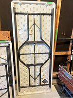 Full view underside of folded white plastic table showing steel frame